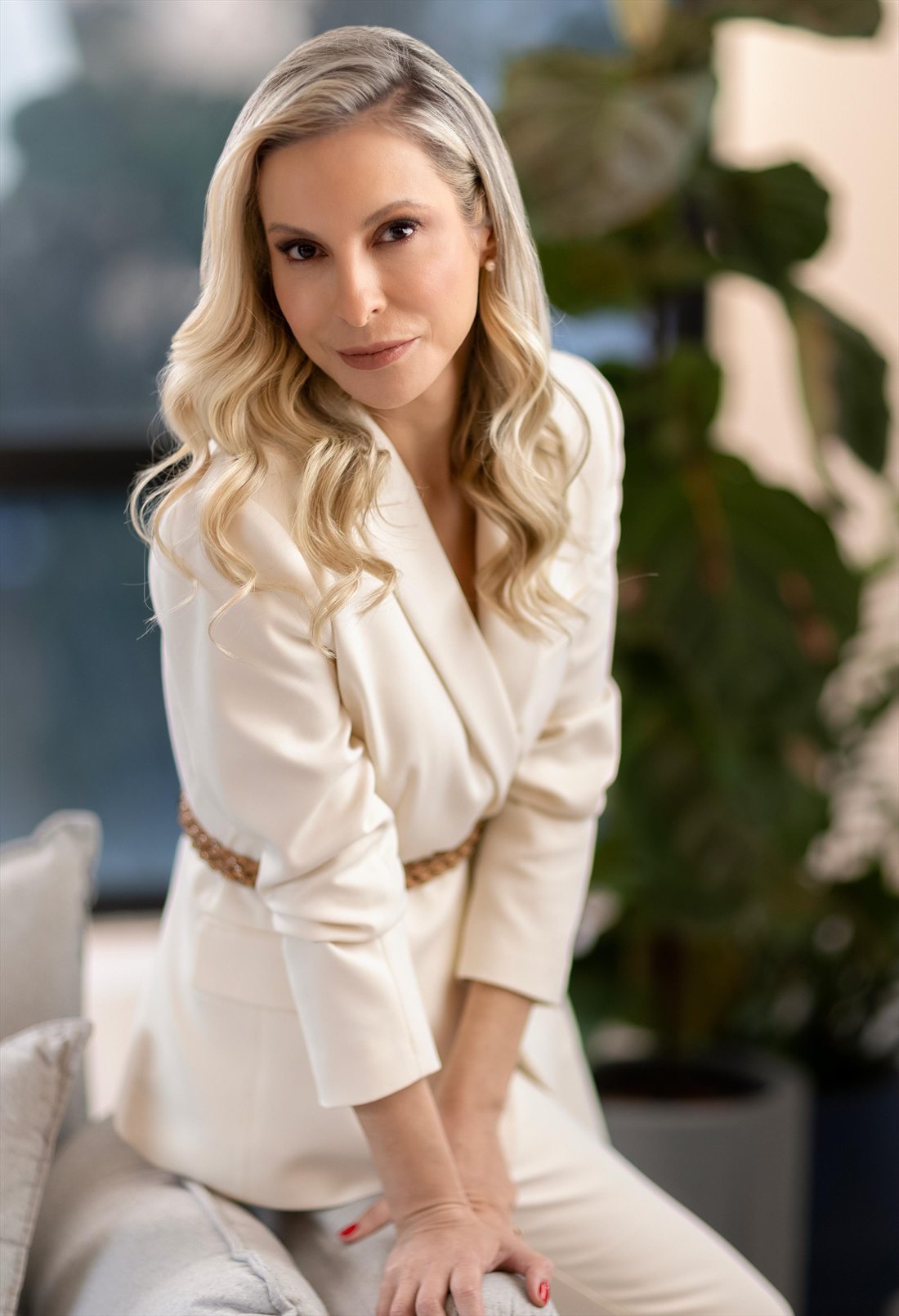 Dra. Agatha Nicolas com blazer creme, apoiada em uma poltrona